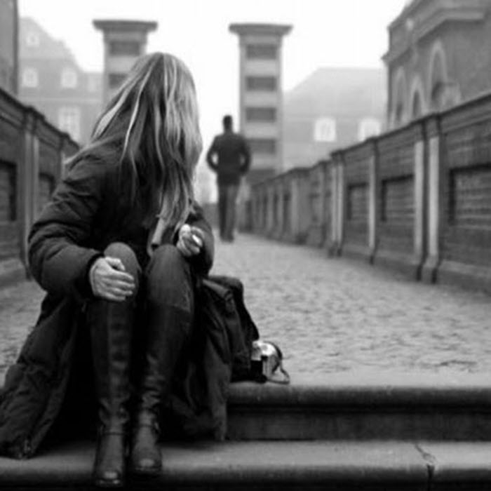 A woman sitting alone on steps as a figure walks away, illustrating avoidant attachment