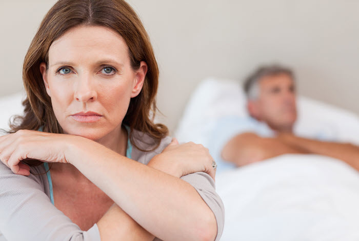 A woman sitting on the edge of the bed with her back to her husband, both awake and silent